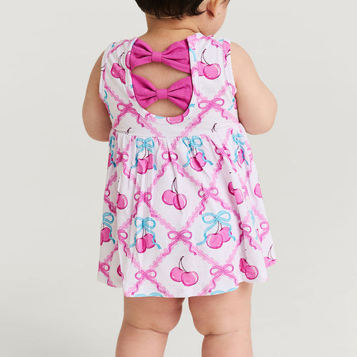 Baby wearing a dress with pink bows and cherries on a white background