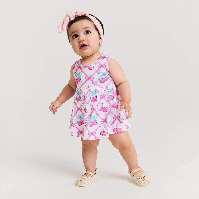 Baby wearing a pink dress with cherry and bow pattern on a white background