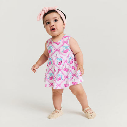 Baby wearing a pink dress with cherry and bow pattern on a white background