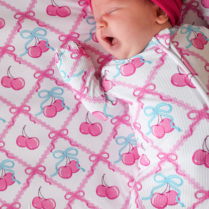 Newborn baby in a pink and white outfit with cherry pattern on a matching blanket.