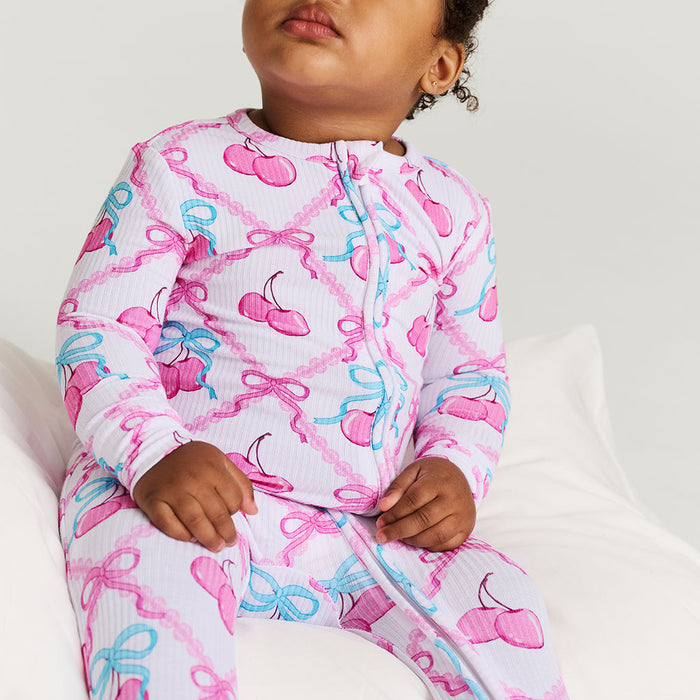 Child wearing a pink and blue bow-patterned one piece on a white background