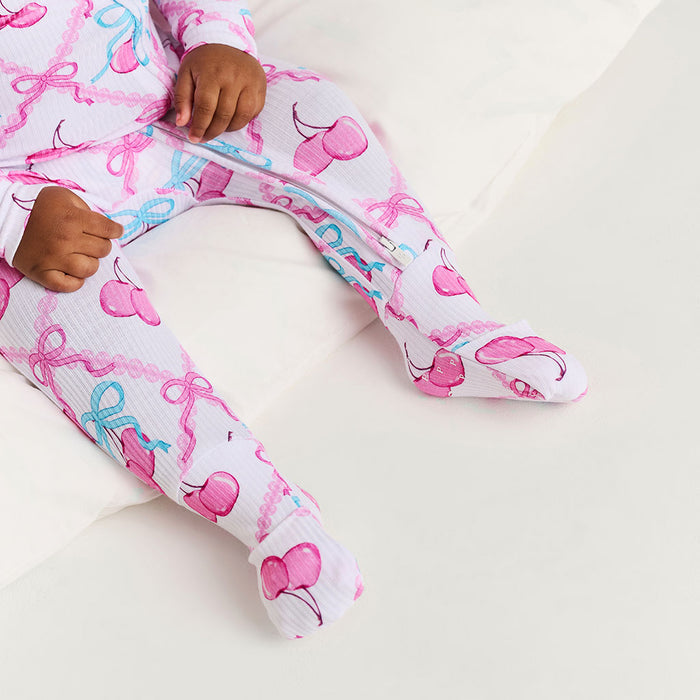 Child wearing pink and white patterned one piece with cherry design on a white background