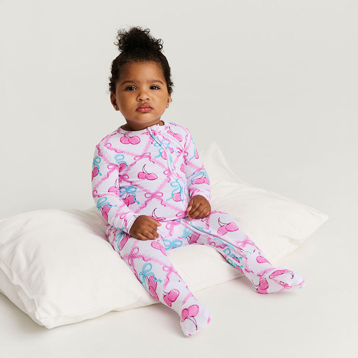 Child wearing a pink and blue patterned one piece sitting on a white bed.