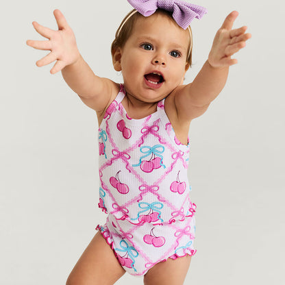 Baby wearing a colorful bummie set with cherries and bows on a plain background