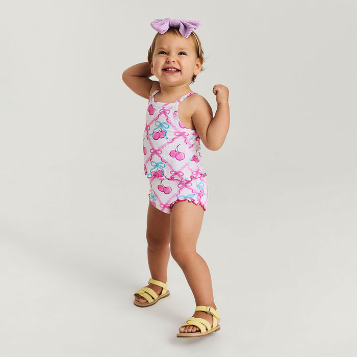 Child wearing a pink bummie set with cherry and bow pattern on a plain background