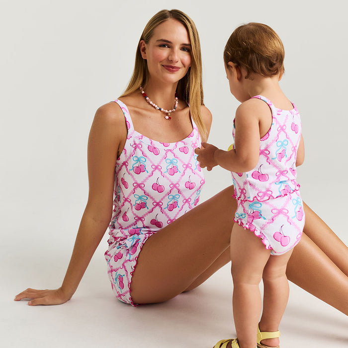 Woman and child wearing matching pink sets with cherries and bow patterns on a white background