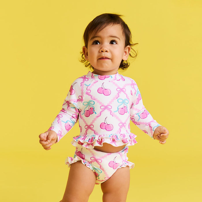 Child wearing a colorful swimsuit set with cherry and bow pattern on a yellow background