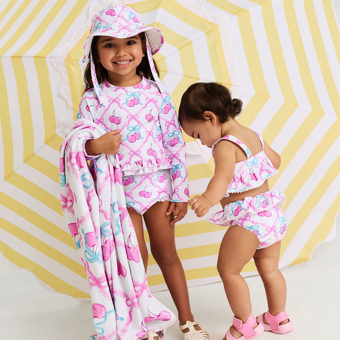 Two children in matching pink and white outfits with a colorful pattern against a yellow and white striped background.