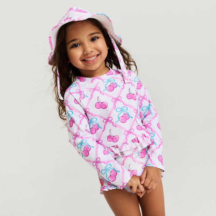 Child wearing a pink rash guard set with cherry and bow pattern on a plain background
