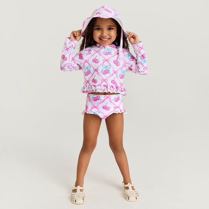 Child wearing a pink cherry-themed rash guard set on a light background