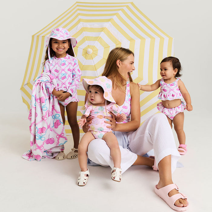 Woman with three children wearing matching pink and white swimwear in front of a yellow and white umbrella.