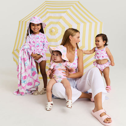 Woman with three children wearing matching pink and white swimwear in front of a yellow and white umbrella.