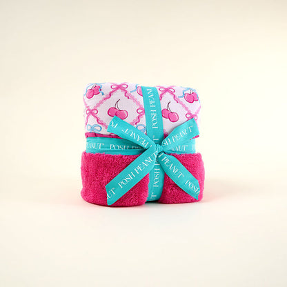 Folded pink blanket with cherry pattern and teal ribbon on a light beige background