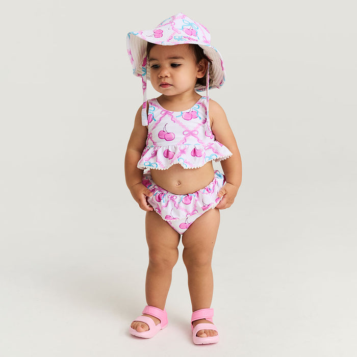 Child wearing a pink and white swimsuit with a matching hat on a light background