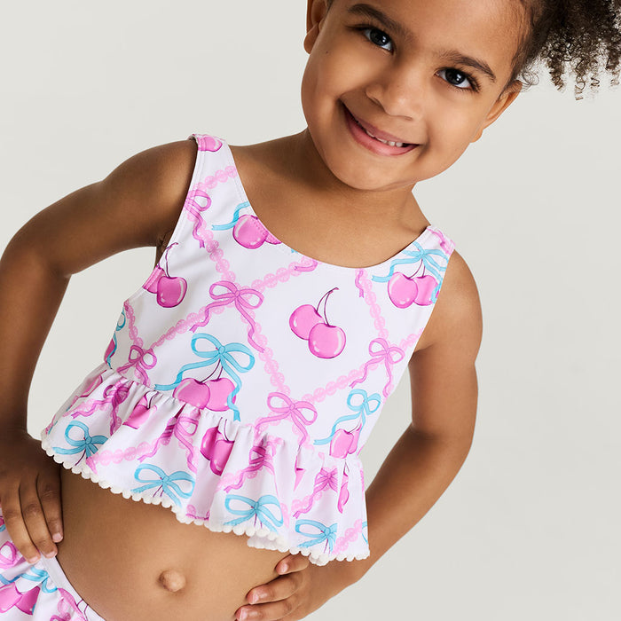 Child wearing a colorful swimsuit with cherries and bows on a plain background