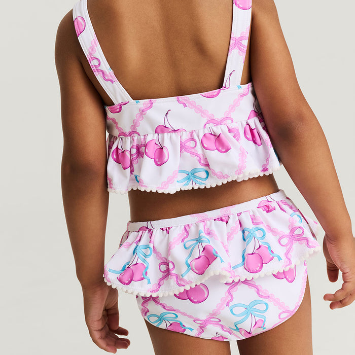 Child wearing a pink and white swimsuit with bow pattern on a plain background