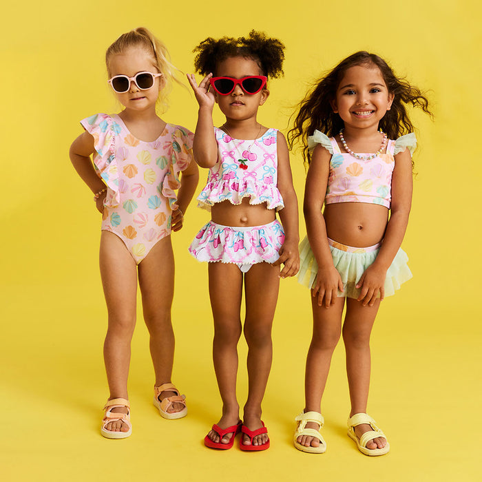 Three young girls wearing colorful swimsuits and sunglasses on a yellow background