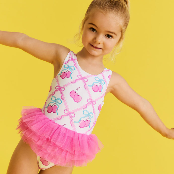 Young girl in a pink and white swimsuit with cherry design on a yellow background