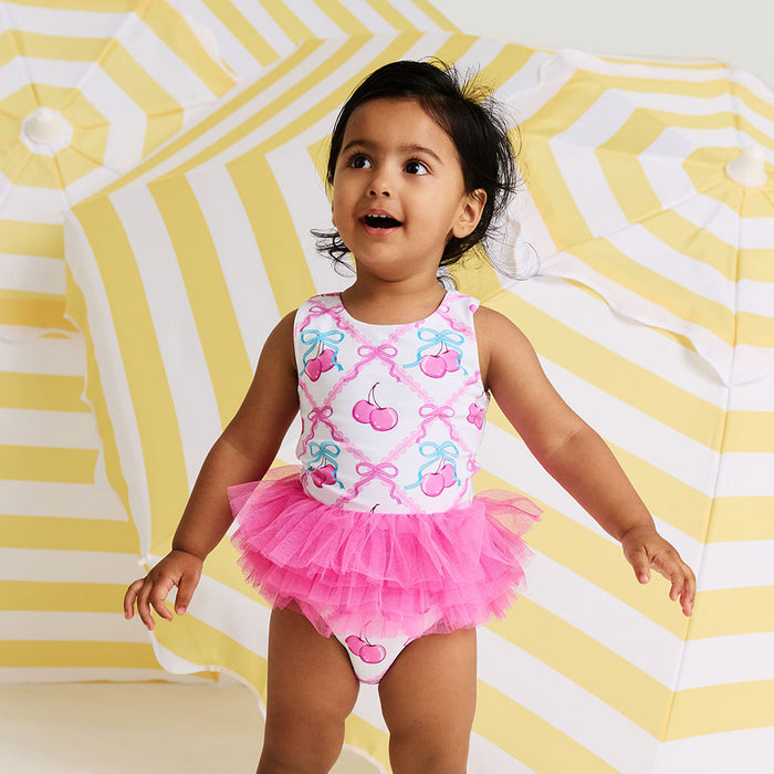Child wearing a pink swimsuit with cherry design on a yellow and white striped background