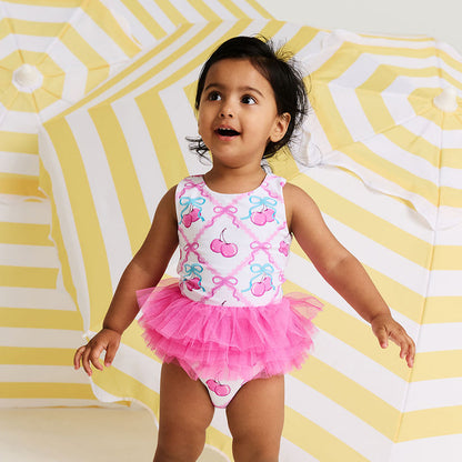 Child wearing a pink swimsuit with cherry design on a yellow and white striped background
