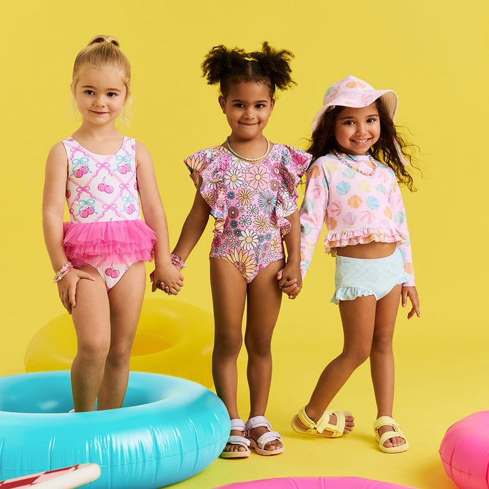 Three young girls in colorful swimwear and accessories on a yellow background
