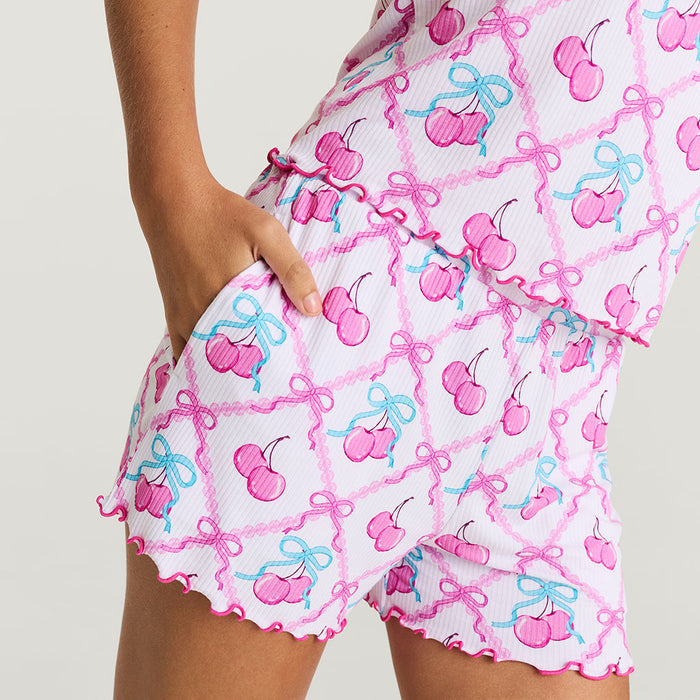 Person wearing a pink and white patterned outfit with cherries and bows on a light background