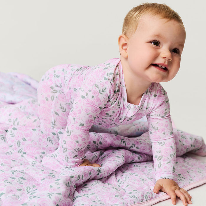 Baby in a pink floral one piece sitting on a white surface