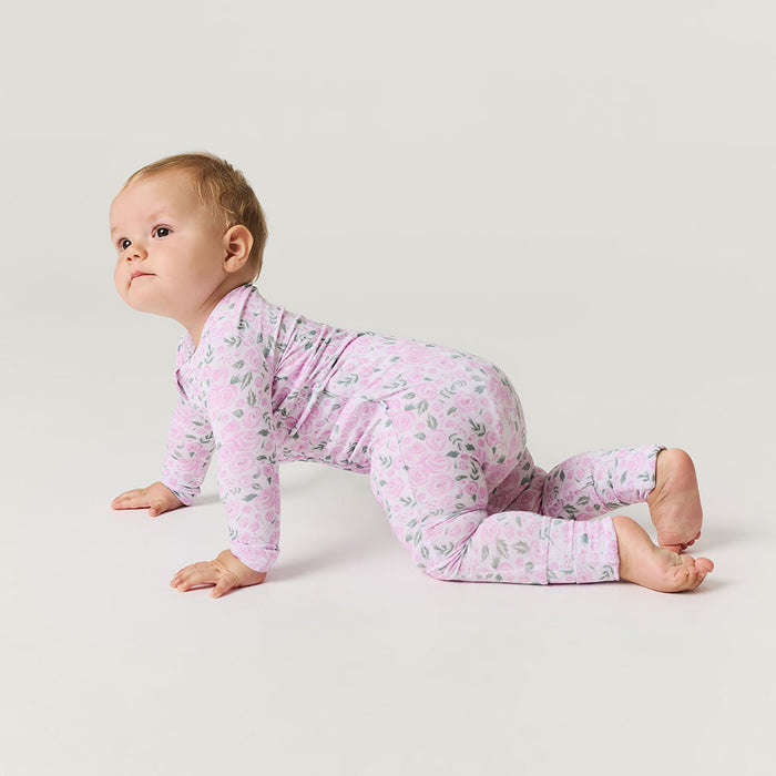 Baby in a pink floral one piece crawling on a light gray background