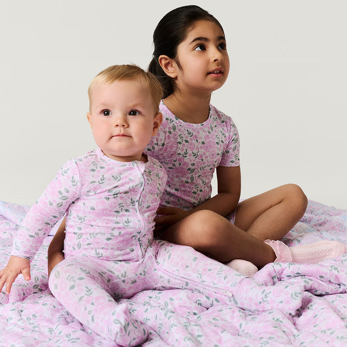 Two children in matching pink pajamas sitting on a bed.