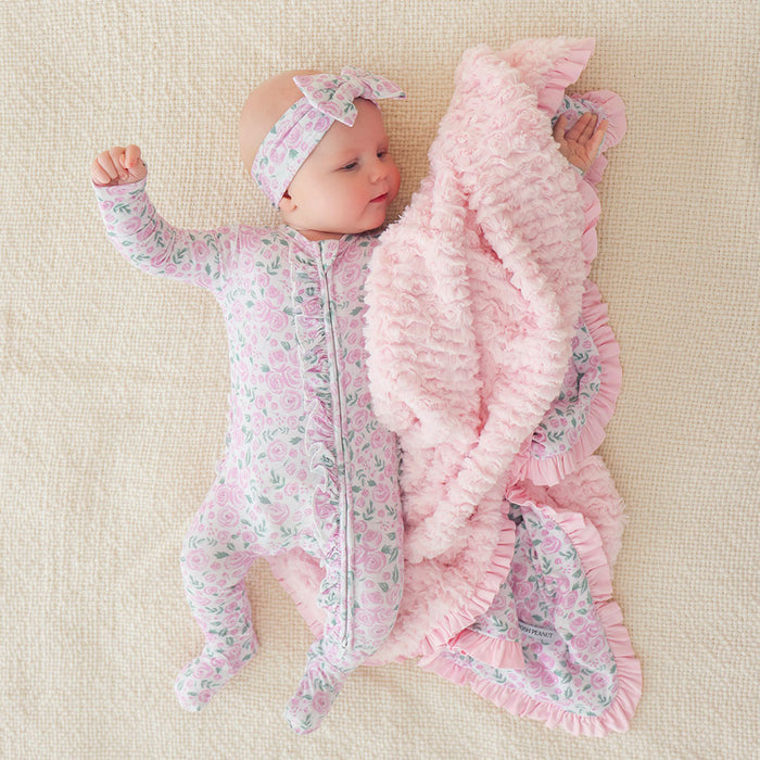 infant laying down on beige colored sheet wearing floral themed print one piece with matching bow headwrap and plush blanket