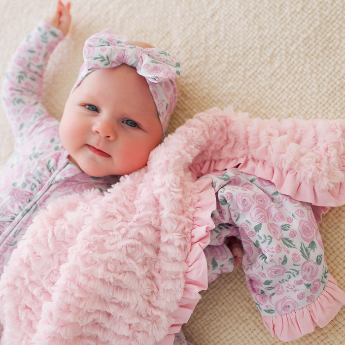 Baby in pink floral outfit lying on a beige surface