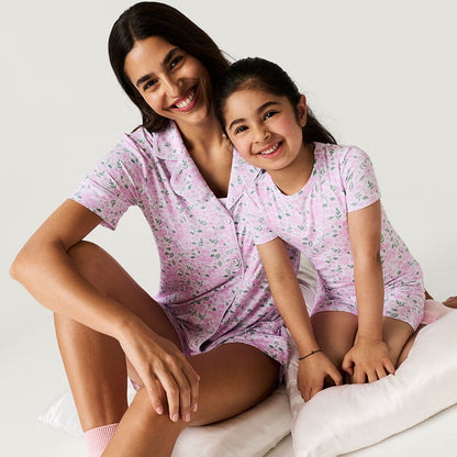 Woman and child wearing matching rose floral printed pajama sets sitting on a white background.