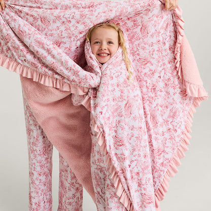 Child wrapped in a pink floral blanket with a person holding it, on a plain background