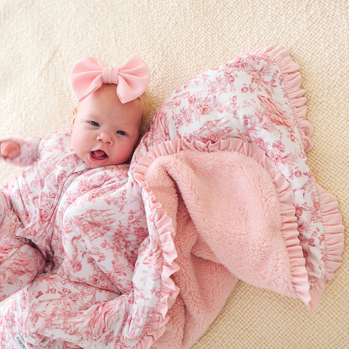 Baby in pink floral outfit with matching bow and blanket on a beige surface
