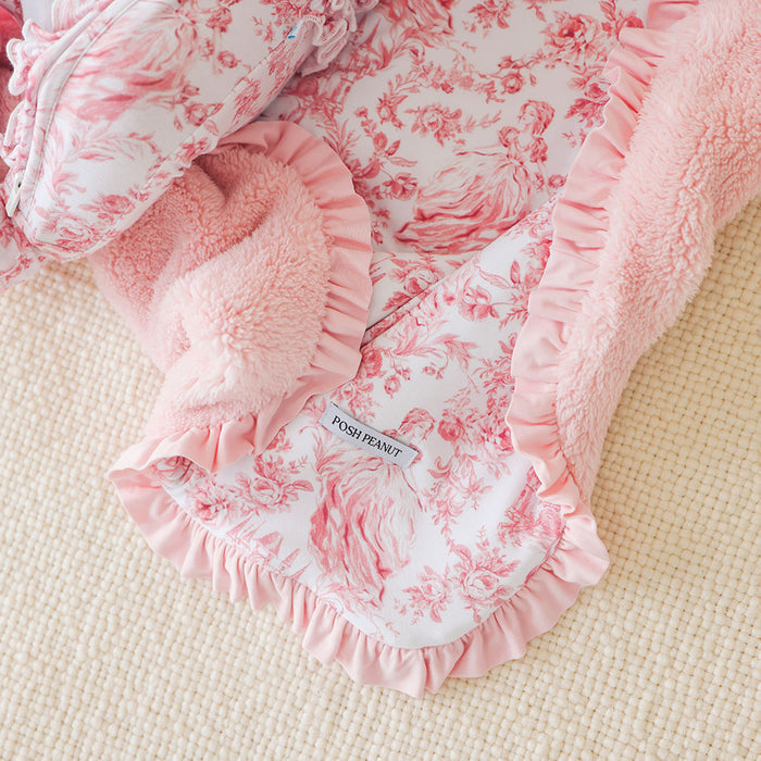 Pink floral baby blanket with ruffles on a beige surface