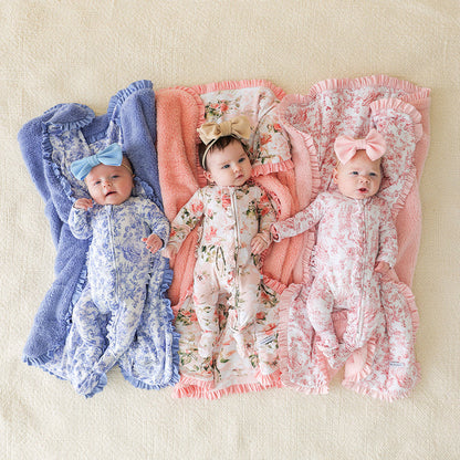Three babies in floral outfits lying on pink and blue blankets.