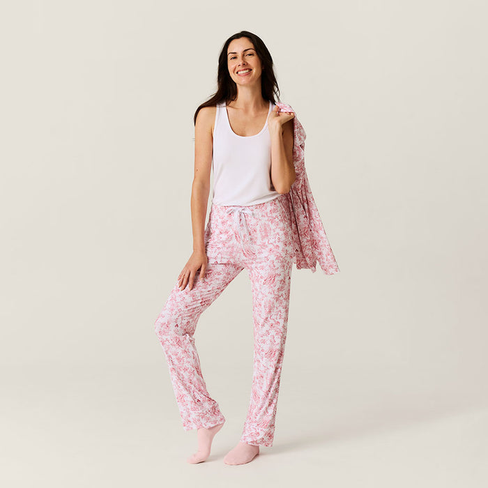 Woman wearing pink floral pajama pants with a white tank top on a light background