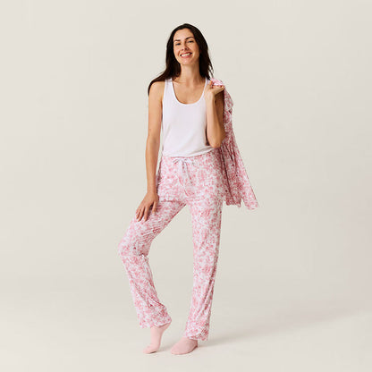 Woman wearing pink floral pajama pants with a white tank top on a light background