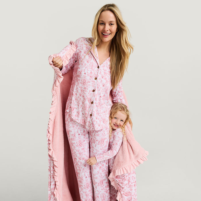 Woman and child wearing matching pink floral pajamas with a blanket on a light gray background