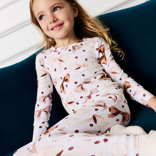 Young girl wearing a white and brown coffee beans and bows pajama set  sitting on a blue couch.