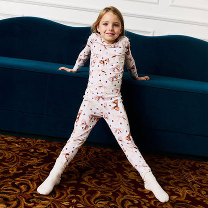 Child wearing a white and brown pajama set with a coffee beans and bows standing on a patterned rug in front of a blue couch.