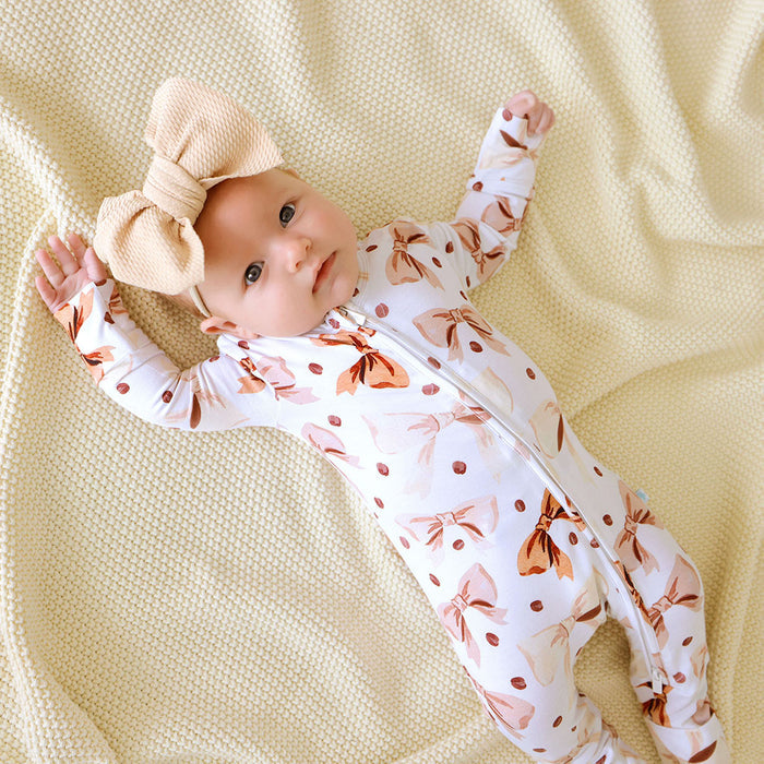 Baby laying down wearing a white and brown cofee beans and bows printed one piece.