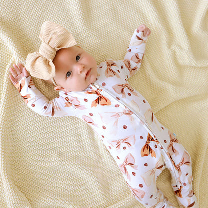 Baby laying down wearing a white and brown cofee beans and bows printed one piece.