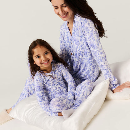 Woman and young girl in matching blue floral pajamas sitting on a bed.
