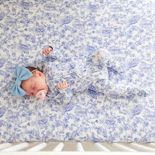 Newborn baby wearing a blue printed one piece lying on a blue floral crib sheet.