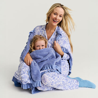 Woman and child in matching blue floral pajamas with a blanket on a light background