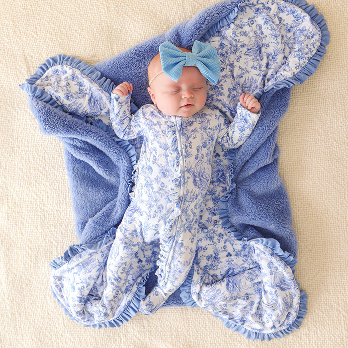Newborn baby wrapped in a blue floral swaddle with a matching bow on a beige background
