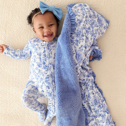 Baby in blue and white floral outfit with matching blanket on beige surface