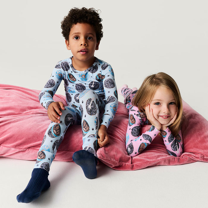 Two children sitting on a pink pillow wearing patterned pajamas.