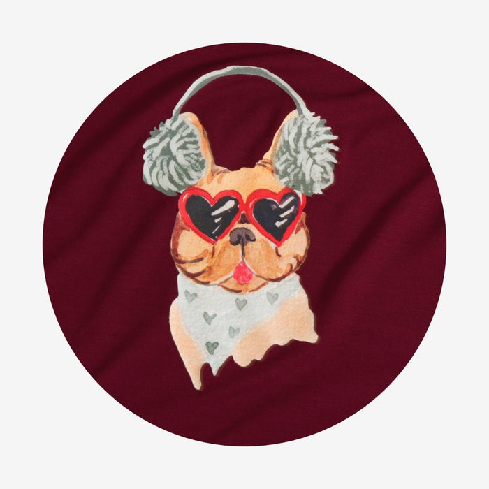 Dog wearing heart-shaped sunglasses and ear muffs on a maroon background